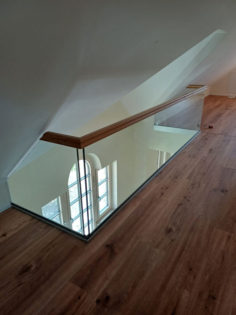Glasbrüstung mit aufgesetztem Holzhandlauf als Galeriegeländer im Dachgeschoss