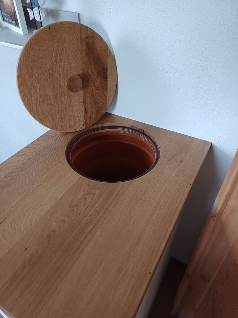 Geöffneter Holzdeckel in einer Eichenplatte mit eingesetztem Keramikbehälter