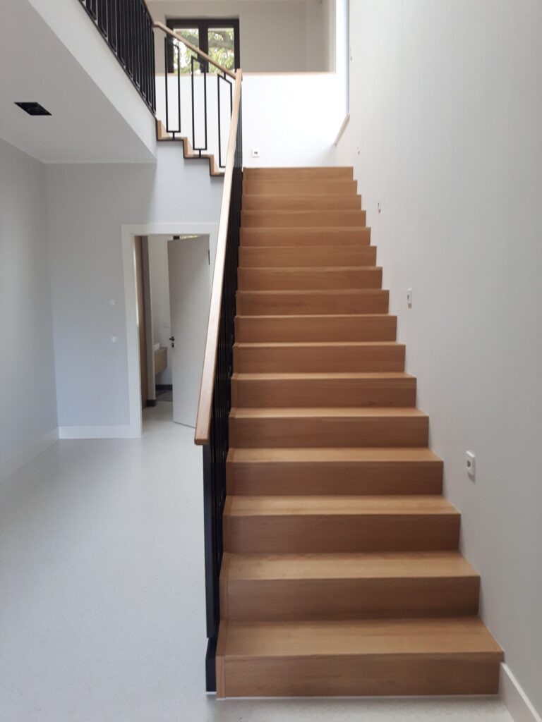 Gerade Faltwerktreppe aus heller Eiche mit schwarzem Stabgeländer und Holzhandlauf