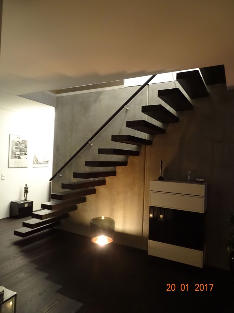 Kragarmtreppe mit dunklen Massivholzstufen, einseitig in einer Betonwand verankert