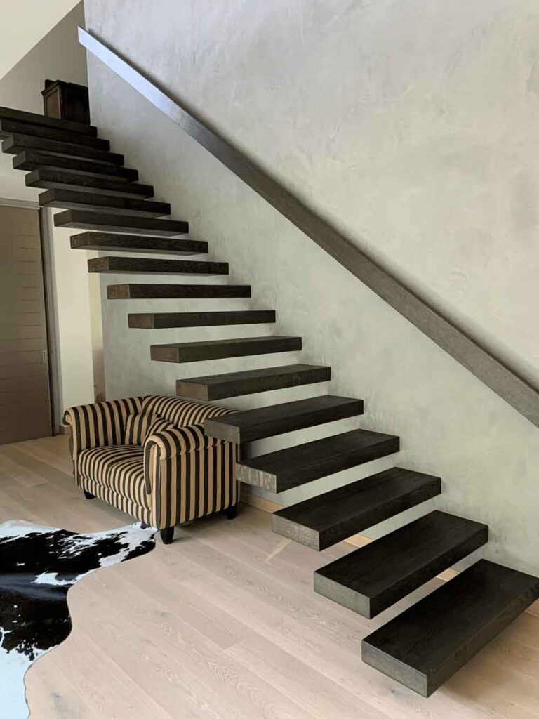 Kragarmtreppe mit dunklen, frei auskragenden Massivholzstufen an einer hellen Wand